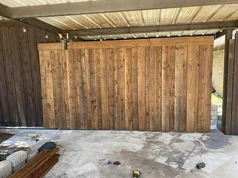 Custom wood plank barn-style garage door installed under a metal carport
