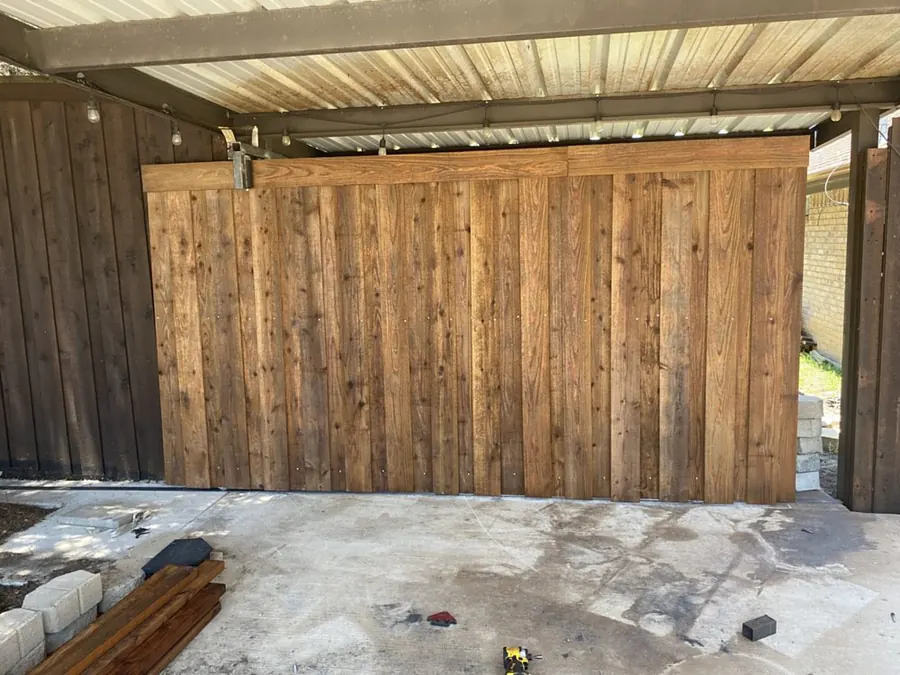 Custom wood plank barn-style garage door installed under a metal carport