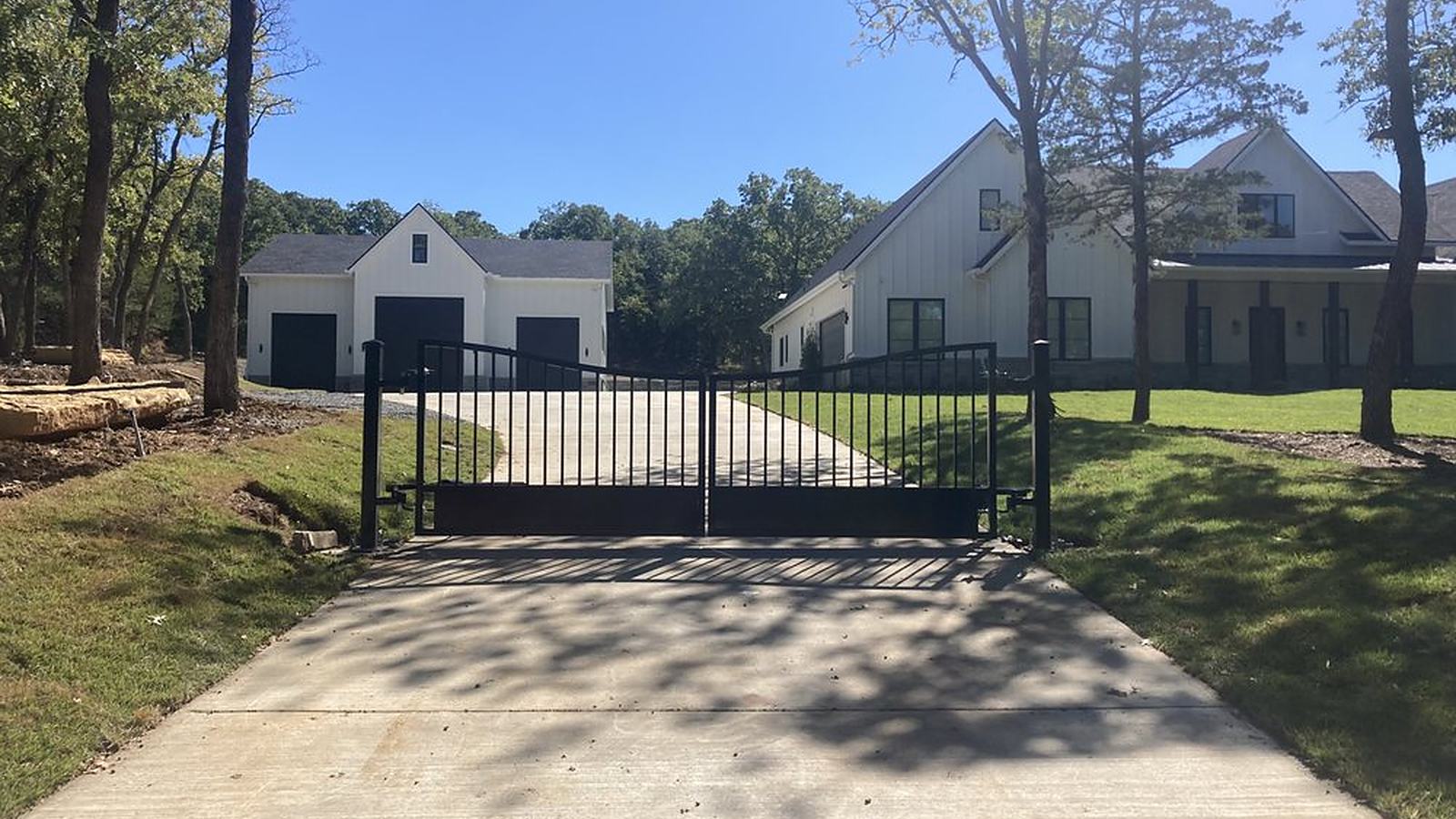Gated residential driveway leading to a home and detached garage with matching black garage doors