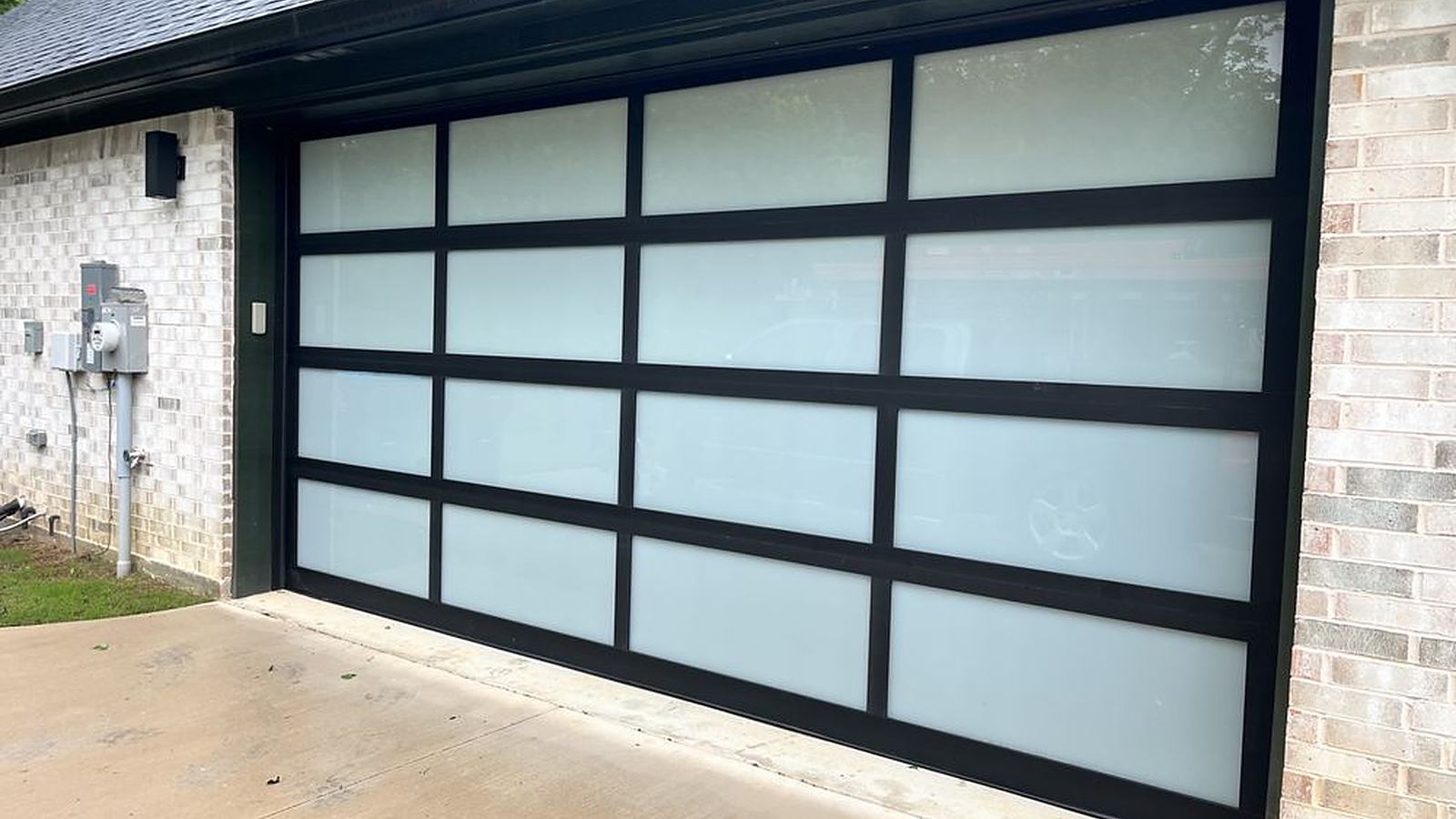 Black aluminum full-view garage door with frosted glass panels on a brick home