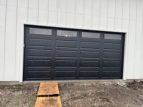 Black raised-panel garage door with top windows replacing an older door