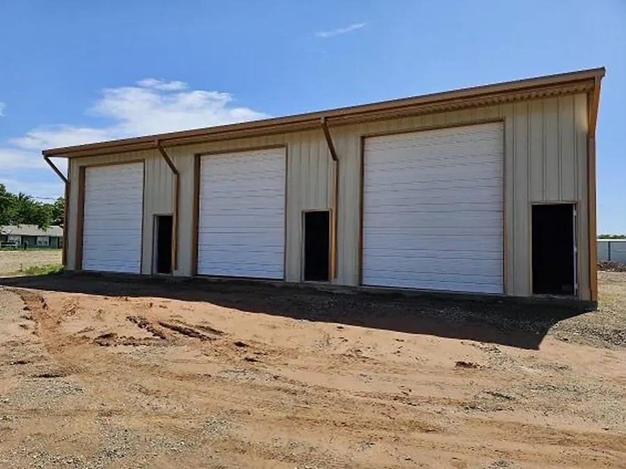 Multi-bay steel building with three white roll-up garage doors and walk-in entries
