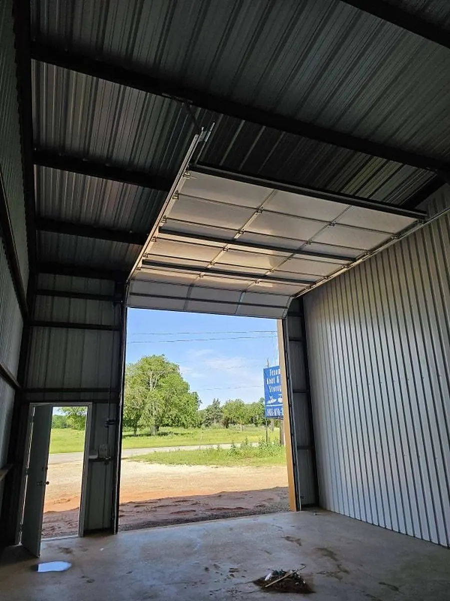 Interior of a steel building with an open overhead garage door looking out to a rural road