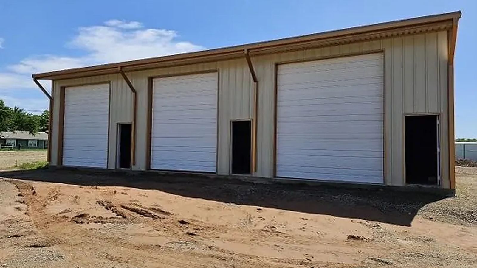 Multi-bay steel building with three white roll-up garage doors and steel walk doors