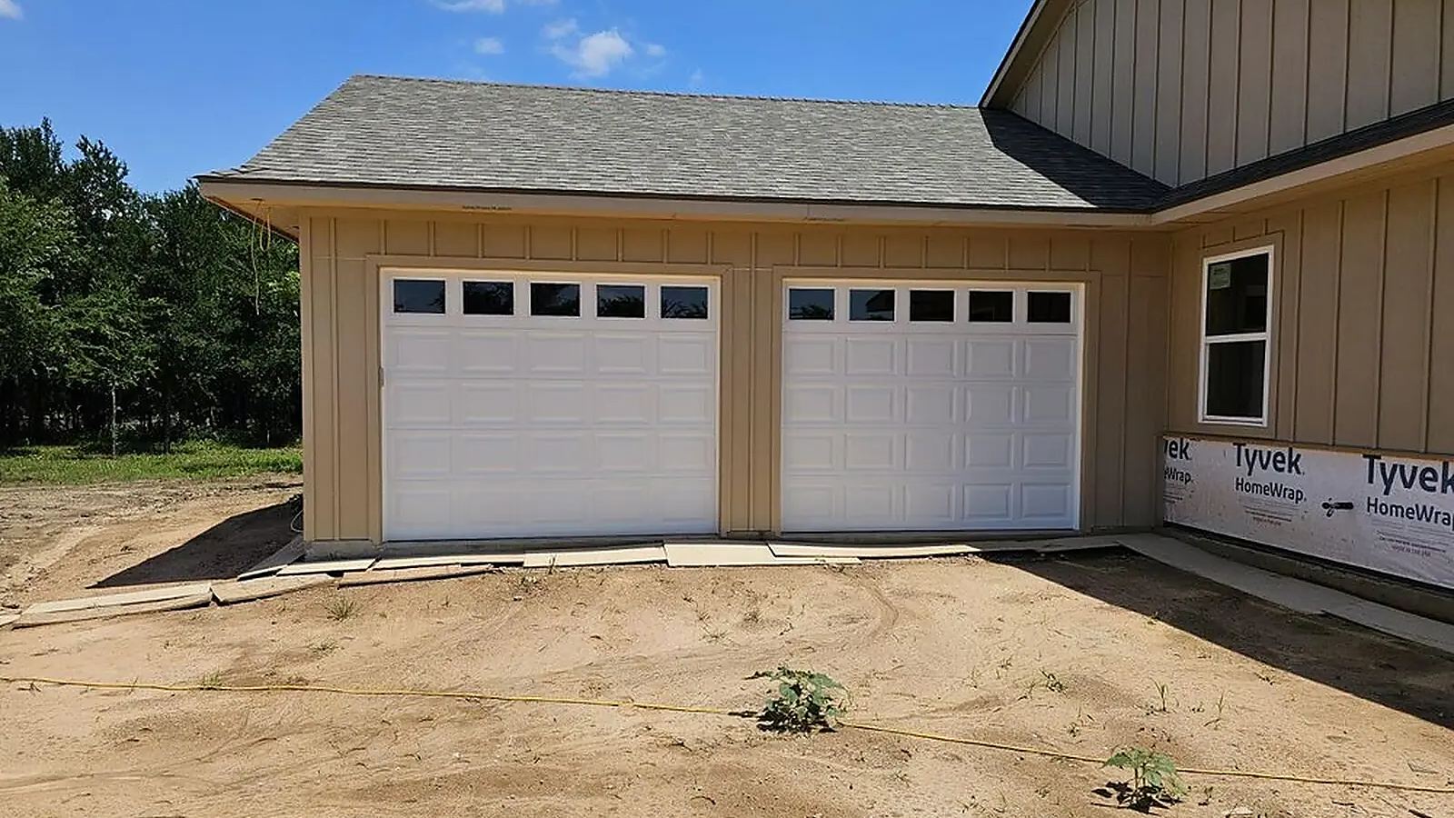 Two white raised-panel garage doors with windows installed on a new construction home