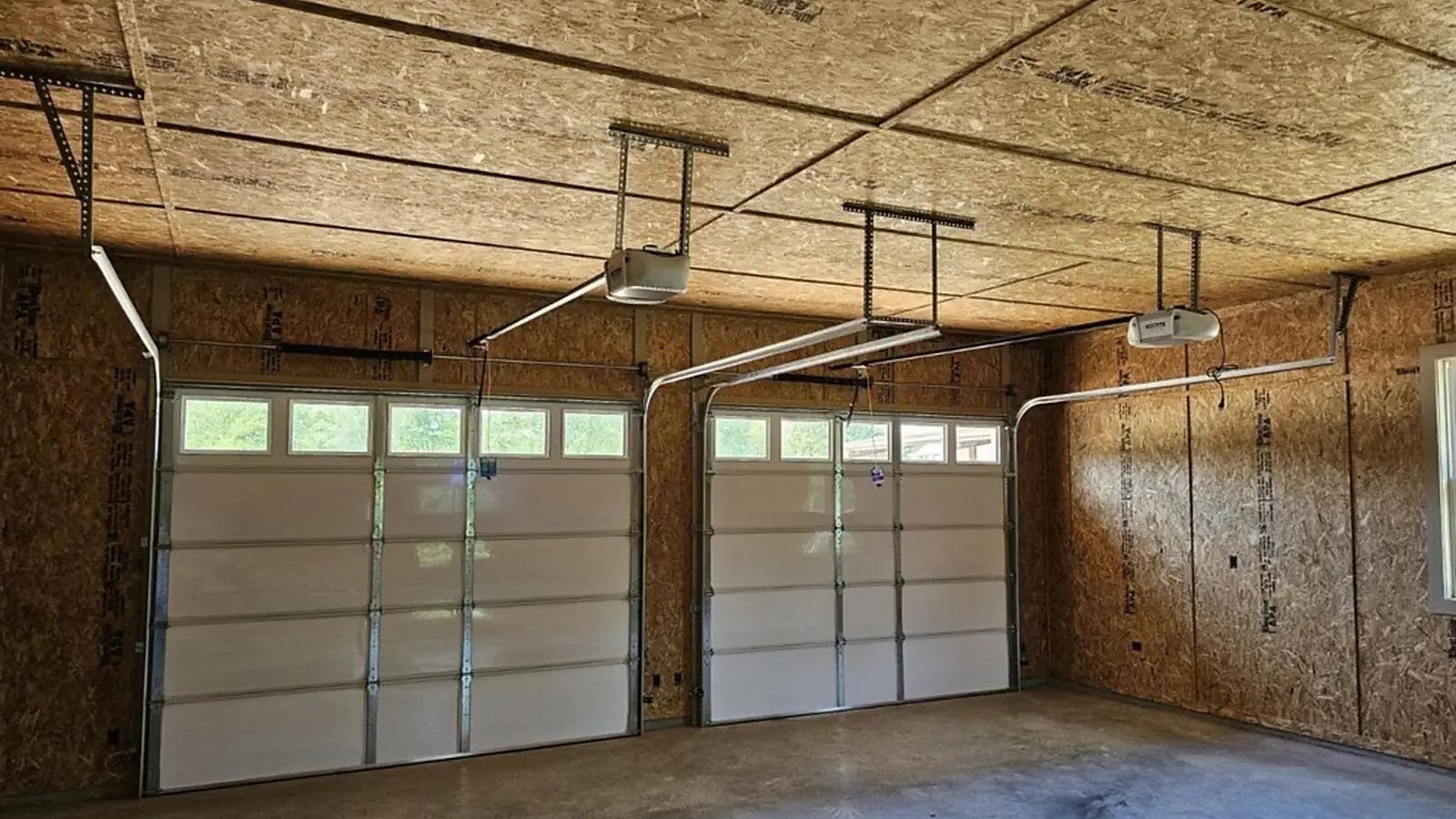 Two ceiling-mounted garage door openers installed above two white garage doors
