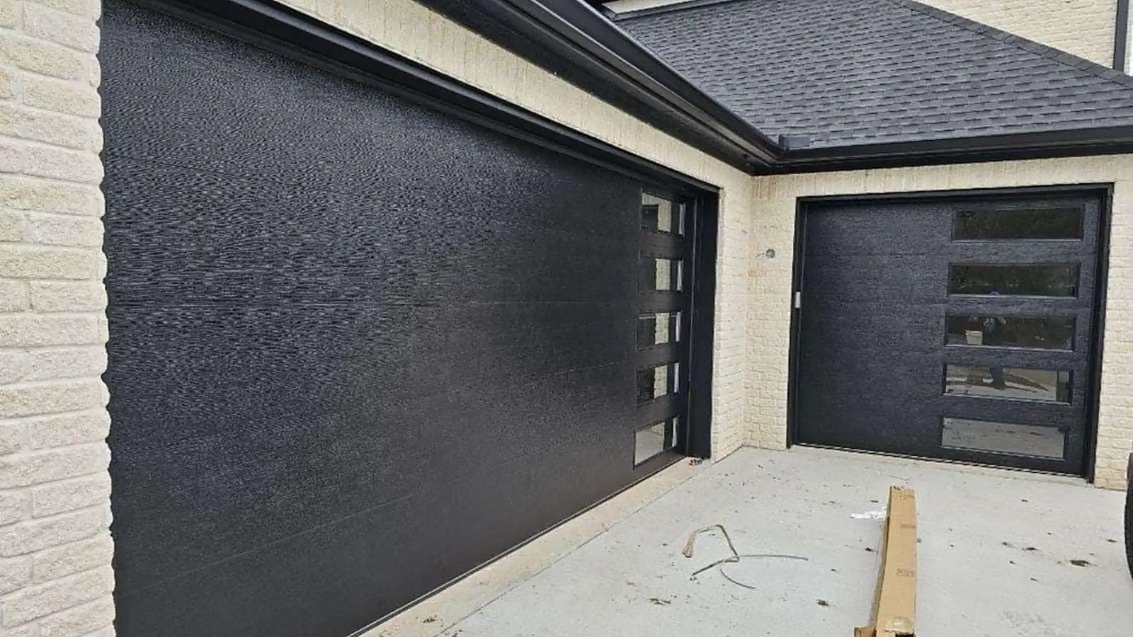 Textured black garage door panel with a vertical glass section on a brick home