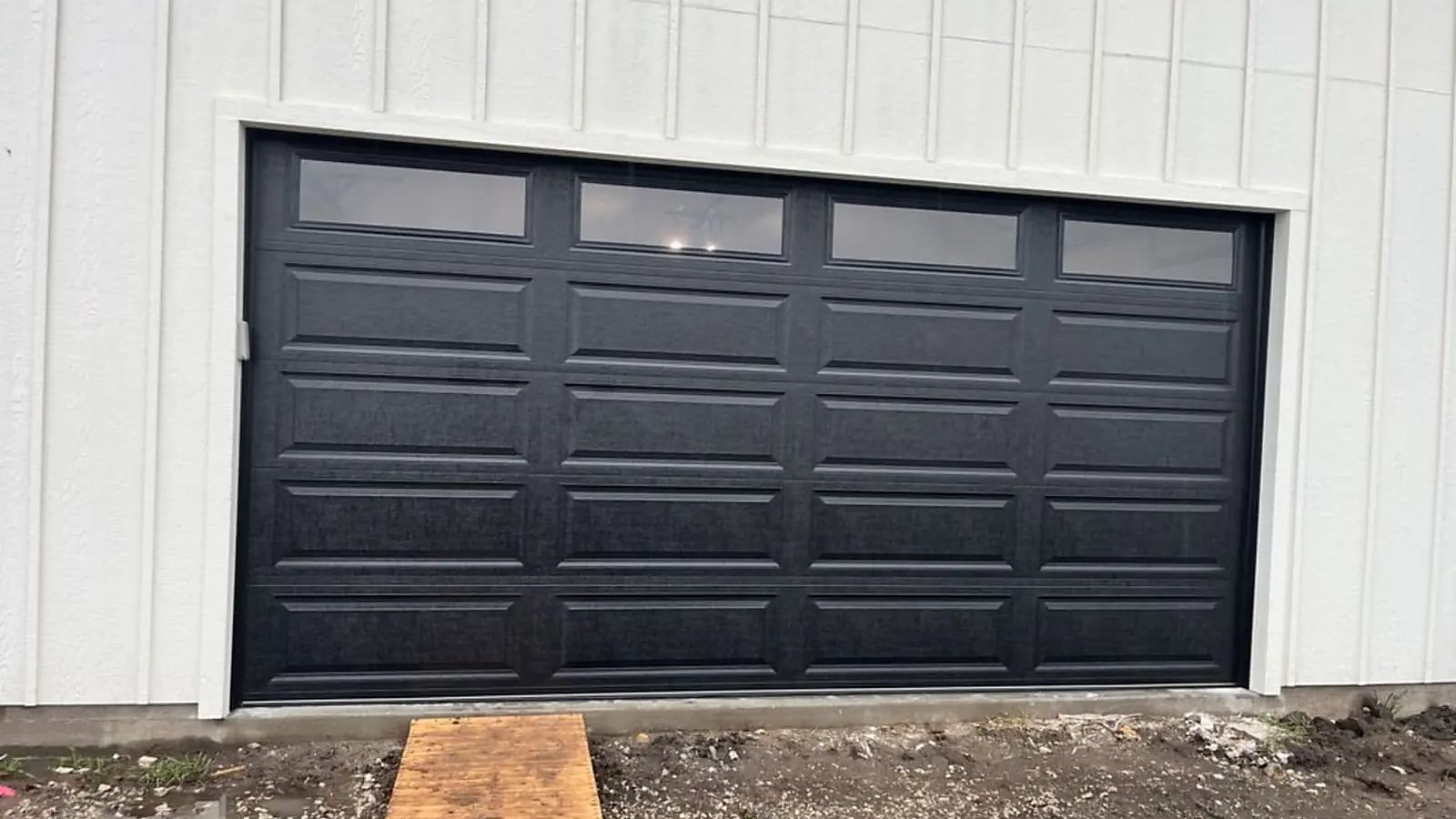 New black raised-panel garage door with top windows replacing an older door on a white facade