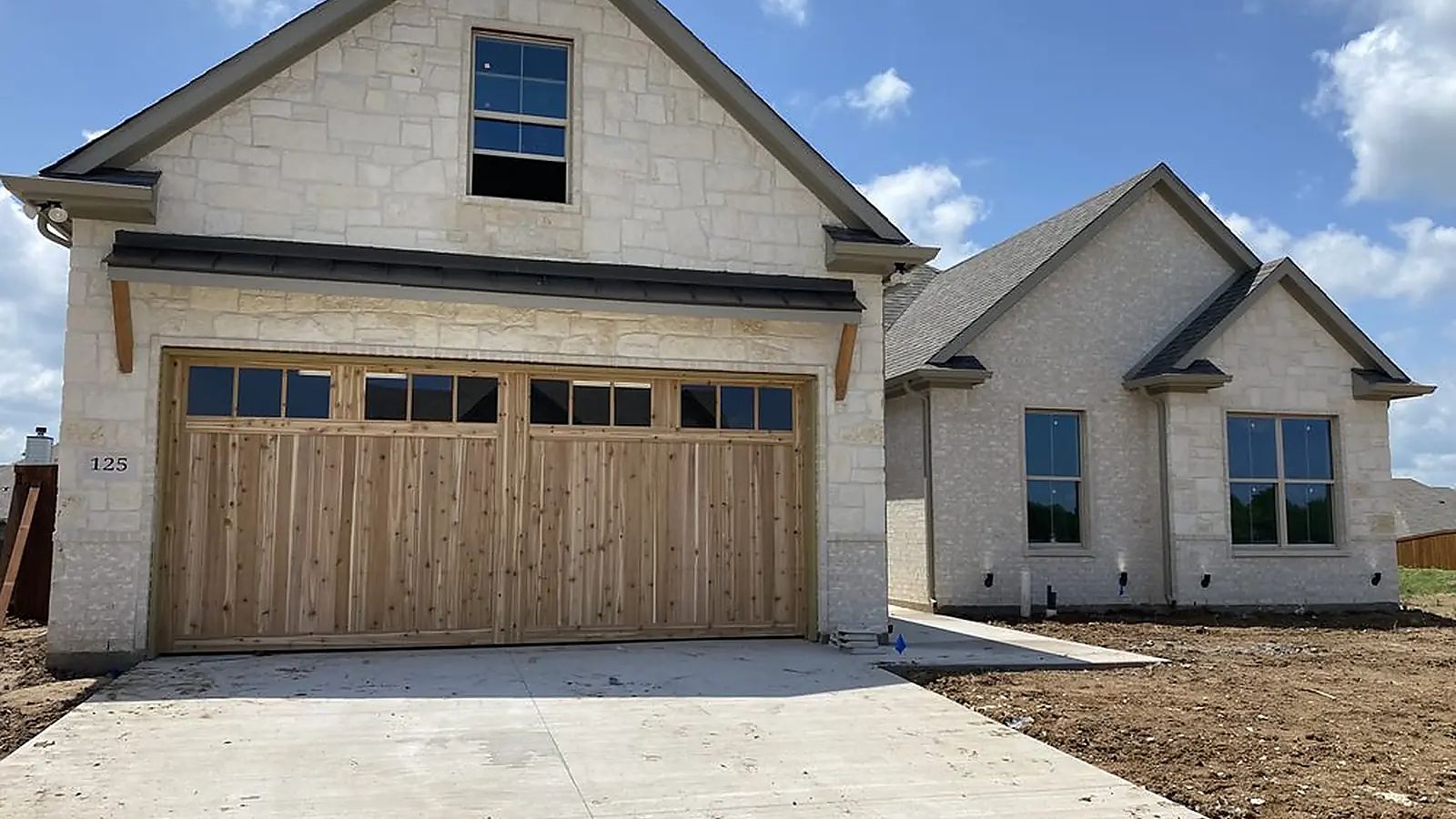 Wood-look carriage garage door with a window row installed on a stone and stucco house