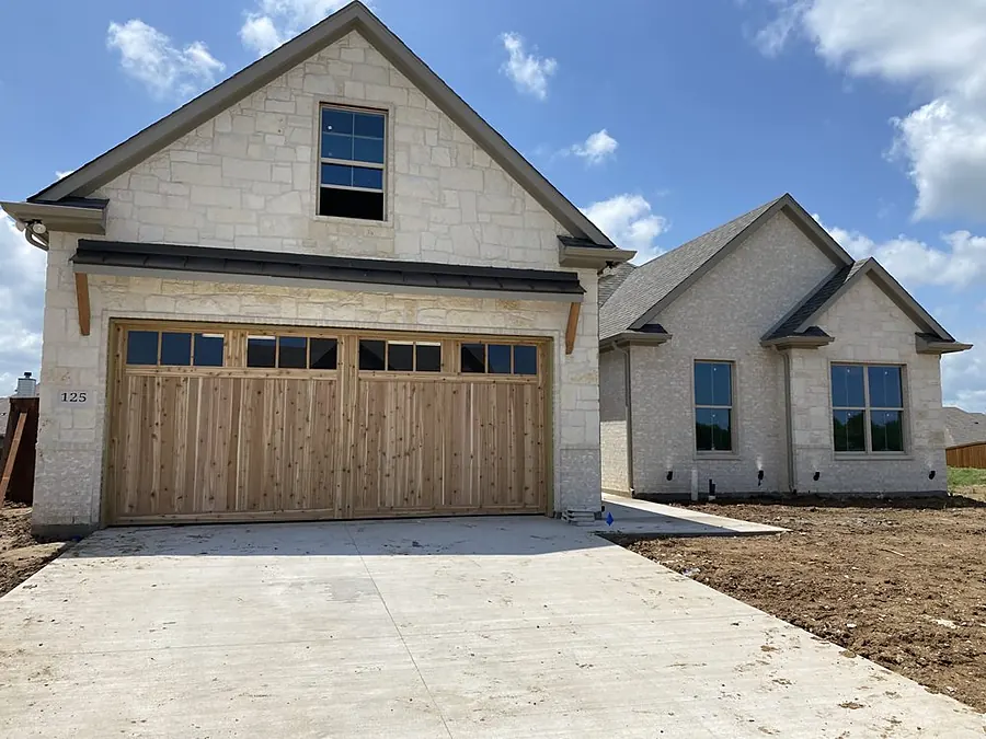 Wood-look carriage style garage door with windows on a stone home with a new concrete driveway